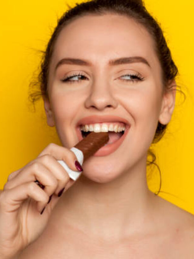 young happy woman enjoying eating chocolate on a yellow background